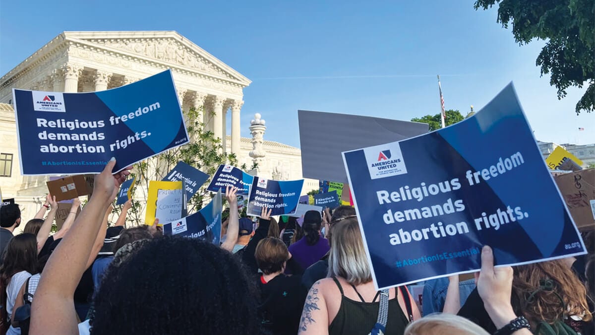 Scaling the summit for religious freedom | Several protesters in front of the Supreme Court hold signs that say "Religious fr