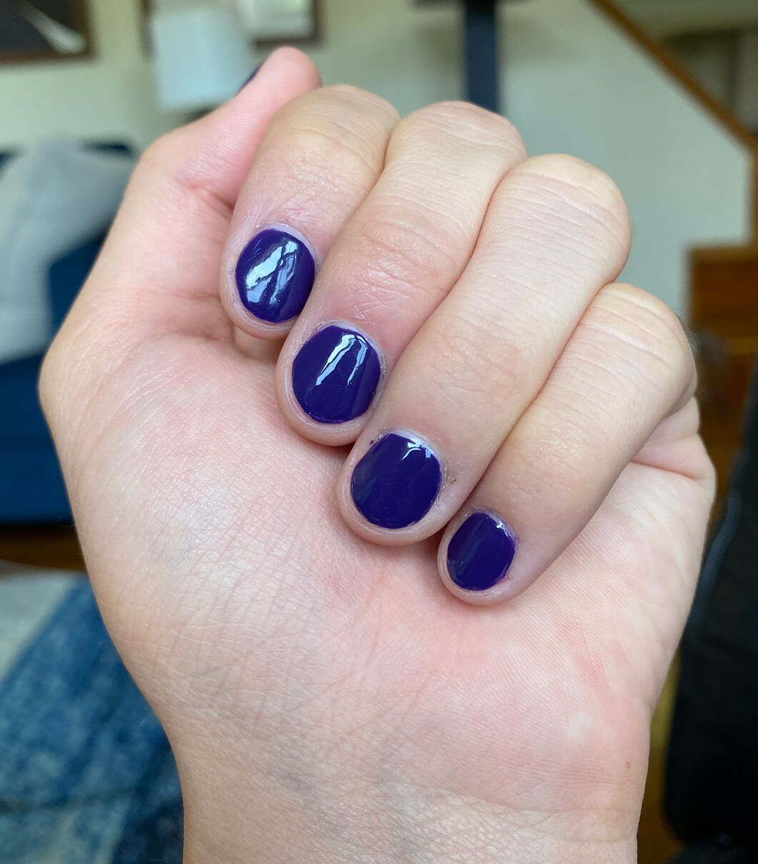 a hand with short nails with dark purple glossy creme nail polish