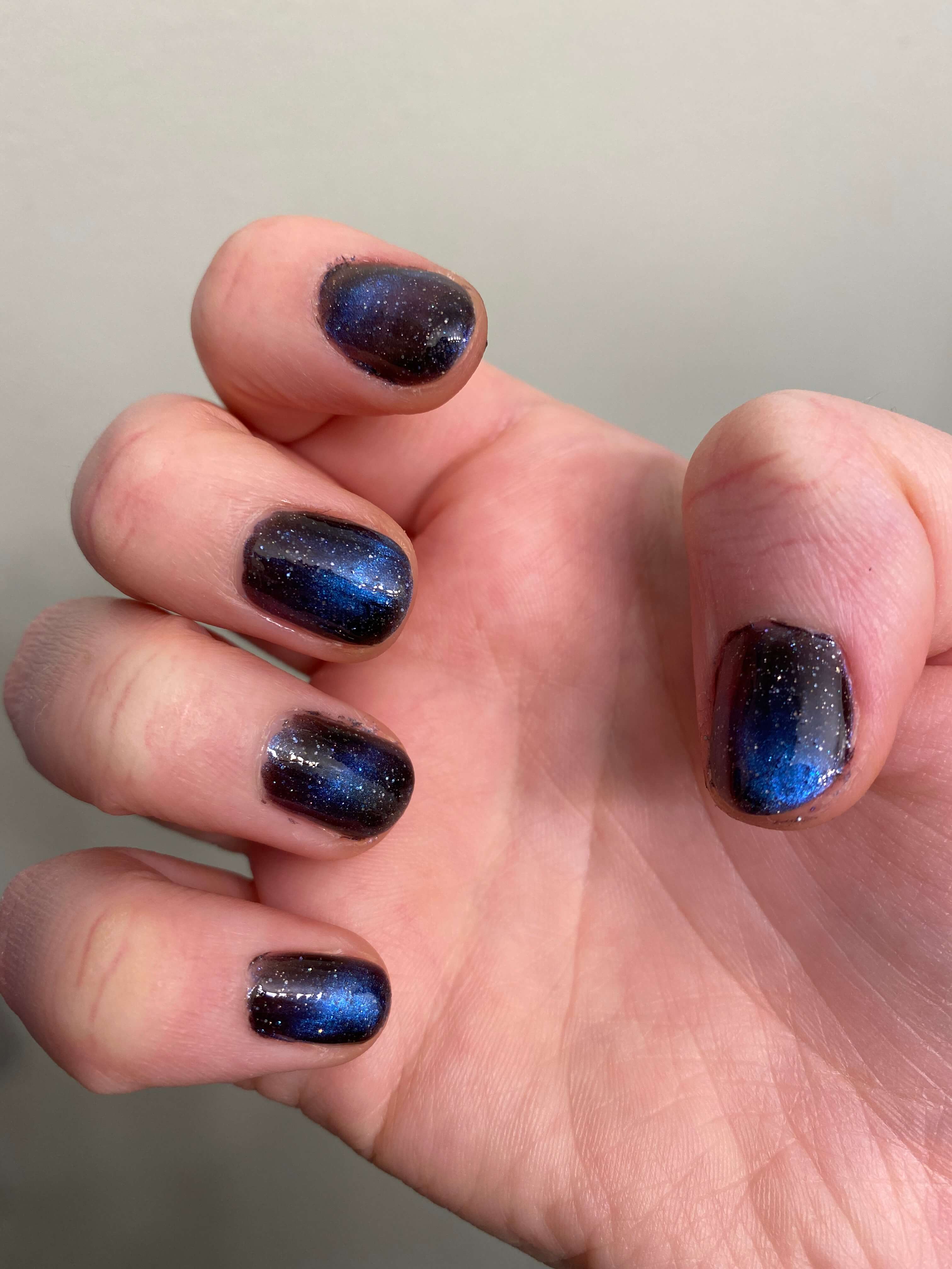 Rebekah's nails with galaxy polish. Her nails are very short, and the application is pretty sloppy. Her hand is in an awkward claw shape.